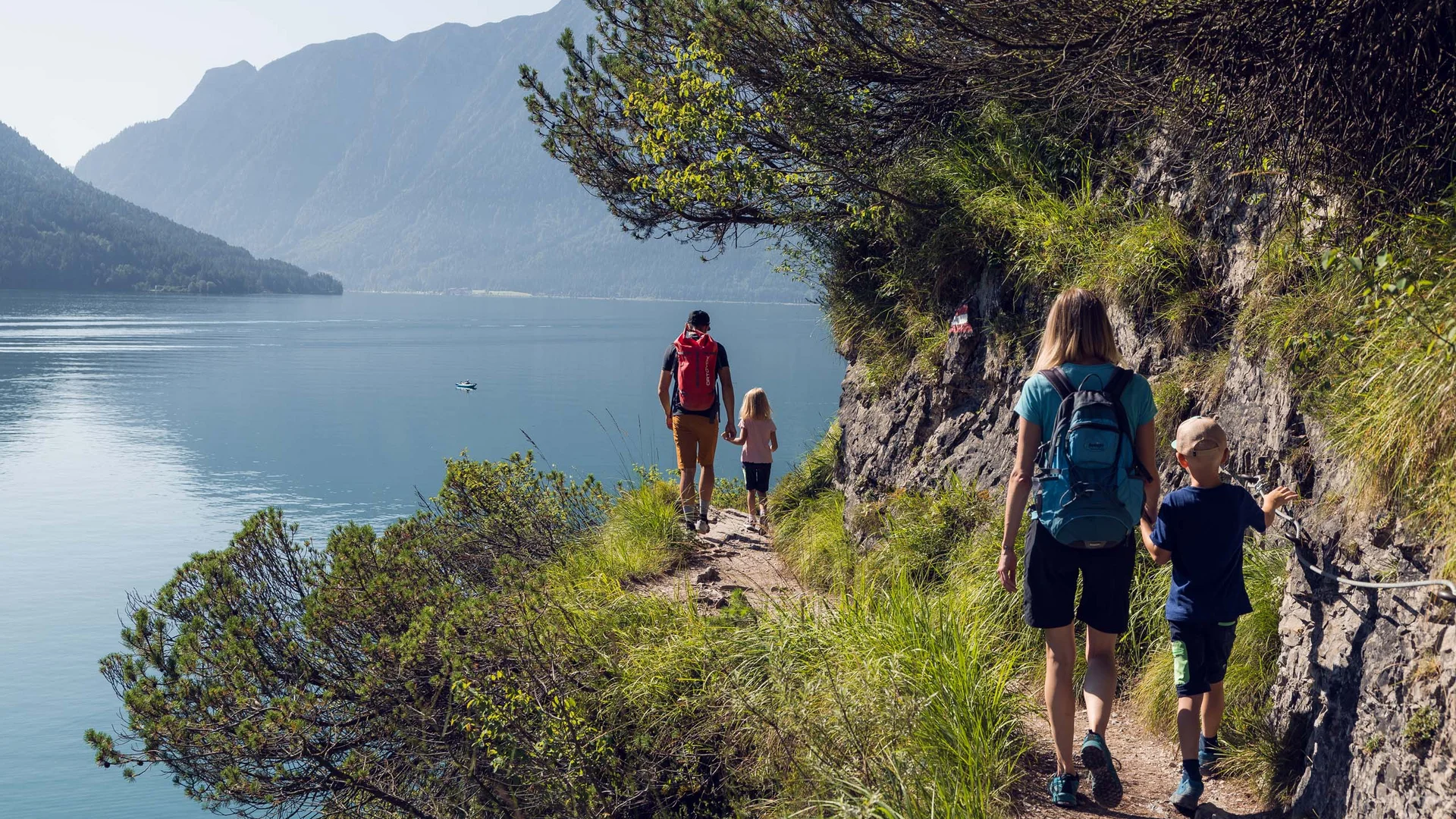 Discover Lake Achensee Family hiking on narrow trail by lake with mountains in the background