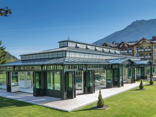 Wiesenhof am Achensee | Das Hotel in Pertisau Historisches Glashaus vor Gebirgslandschaft und Hotelgebäude bei klarem Himmel