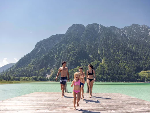 Discover Lake Achensee Family walking on a pier at the lake with forested mountains in summer