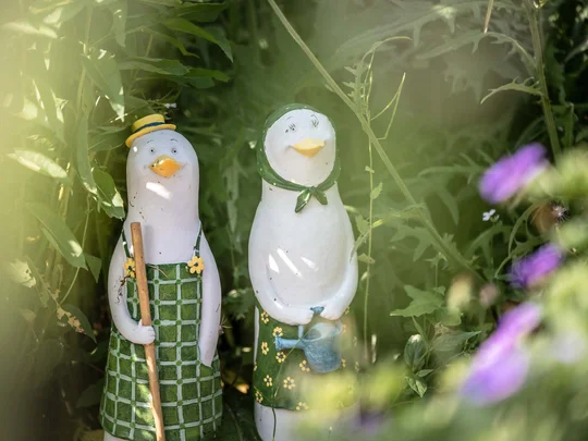 Wiesenhof in Pertisau: the Entner family and team Two goose statues holding garden tools among green plants