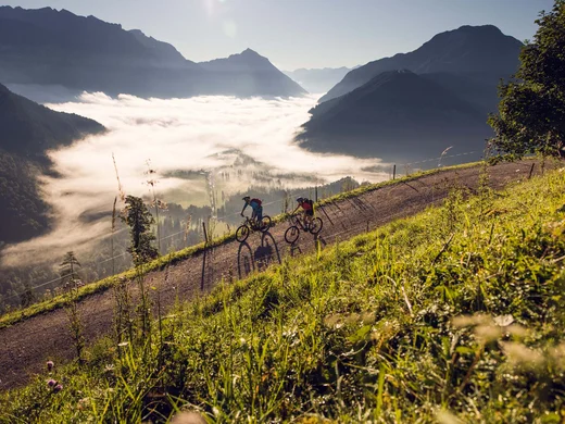 Discover Lake Achensee Two mountain bikers on a trail with fog filling the valley below
