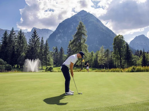 Discover Lake Achensee Man putting on golf green with mountainous background and fountain