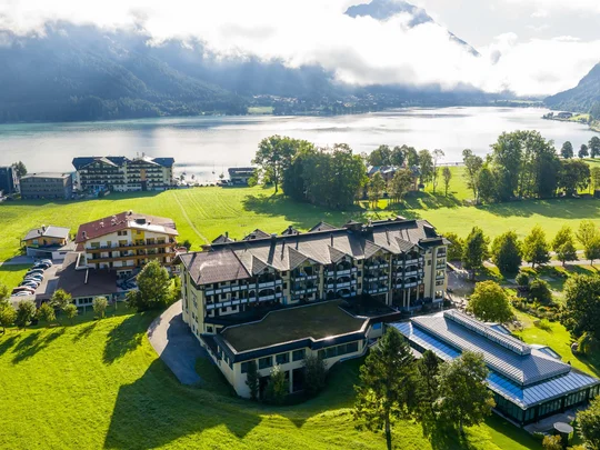 Wiesenhof am Achensee | Das Hotel in Pertisau Luftaufnahme eines Hotels am See mit Bergen und bewölktem Himmel im Hintergrund