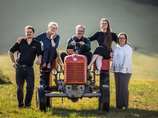 Wiesenhof in Pertisau: the Entner family and team Five people standing and sitting on a red tractor in a grassy field