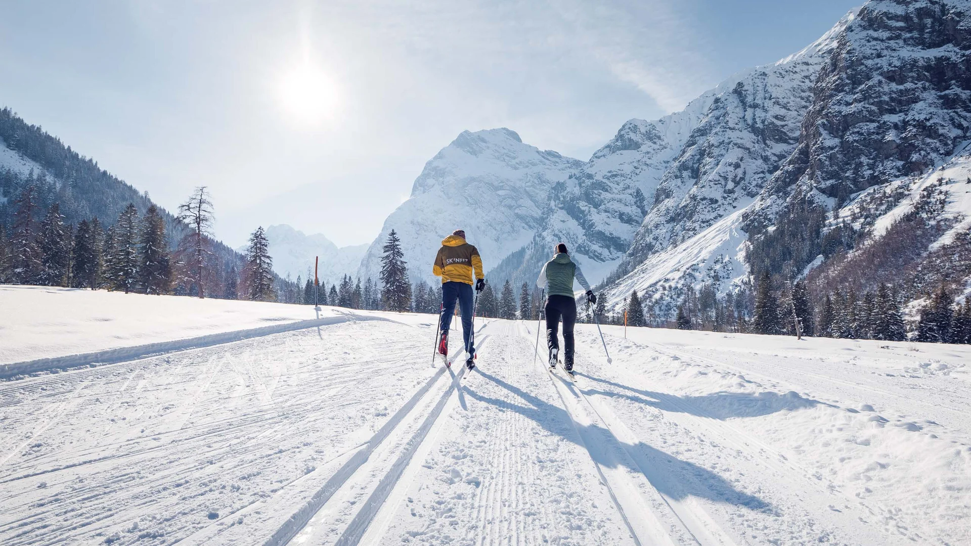 Discover Lake Achensee Two skiers cross-country skiing on snowy mountain landscape in sunny weather