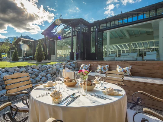 Wiesenhof in Pertisau: the Entner family and team Set outdoor dining table with chairs and glass building facade in sunlight