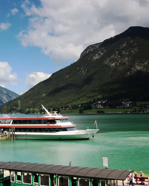 Wiesenhof am Achensee | Das Hotel in Pertisau Grüner historischer Zug und Ausflugsboot am See mit Bergen und blauem Himmel
