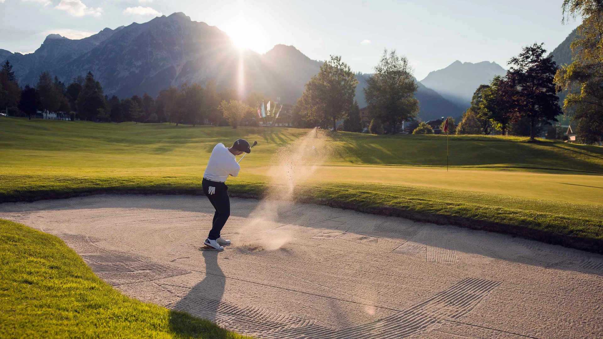 Discover Lake Achensee Golfer hitting ball from sand bunker with mountains and sun in background