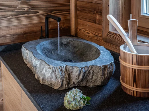 Wiesenhof am Achensee | Das Hotel in Pertisau Steinwaschbecken mit Wasserhahn und Holzgefäß auf schwarzer Arbeitsplatte
