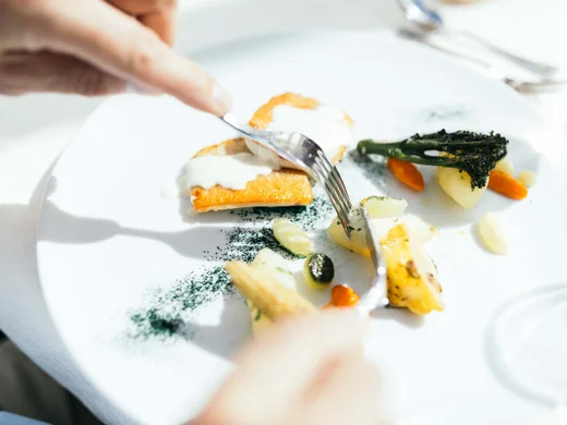 Wiesenhof am Achensee | Das Hotel in Pertisau Person schneidet feines Gourmetgericht mit Gemüse und Sauce auf weißem Teller