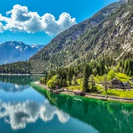 Eure Fragen – unsere Wiesenhof Antworten Bergsee mit blauem Himmel, Wolken und Häusern am Ufer