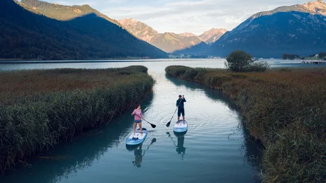 Wiesenhof from all perspectives Two people paddleboarding on a lake surrounded by reeds and mountains