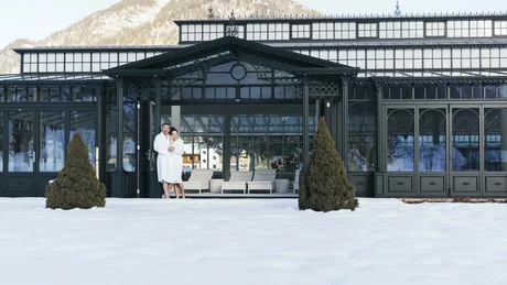 Wiesenhof from all perspectives Couple in bathrobes outside winter hotel with snowy garden and mountains