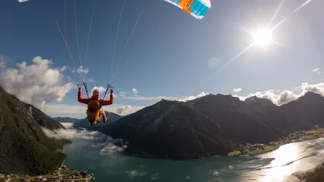 Wiesenhof from all perspectives Person paragliding over mountain lake with sun and clouds