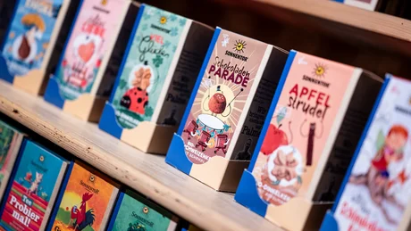 Wiesenhof from all perspectives Row of colorful Sonnentor gift boxes on wooden shelf