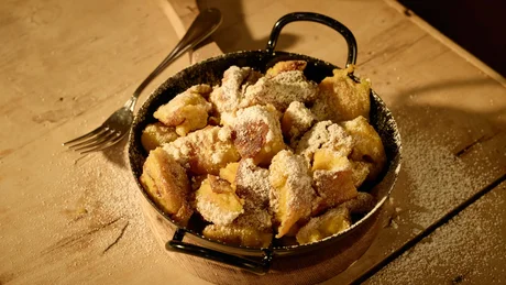Wiesenhof from all perspectives Kaiserschmarrn in a pan sprinkled with powdered sugar on wooden surface