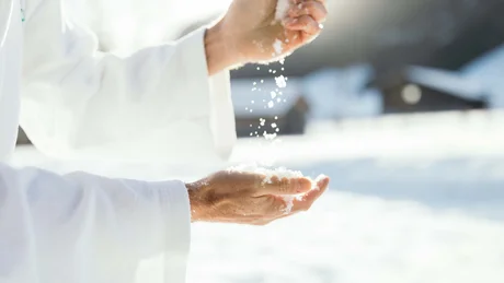 Wiesenhof from all perspectives Hands in white coat holding and letting snow fall in bright light