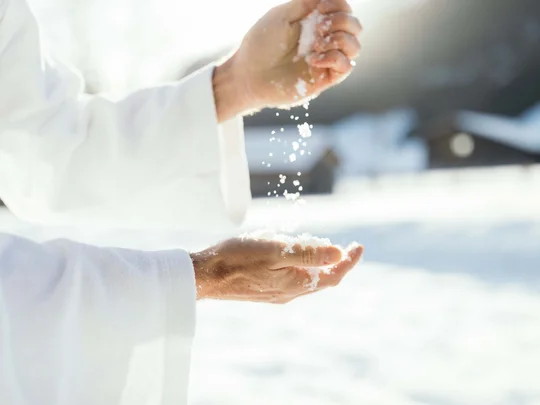 Wiesenhof – your spa hotel in Tyrol Hands in white coat holding and letting snow fall in bright light