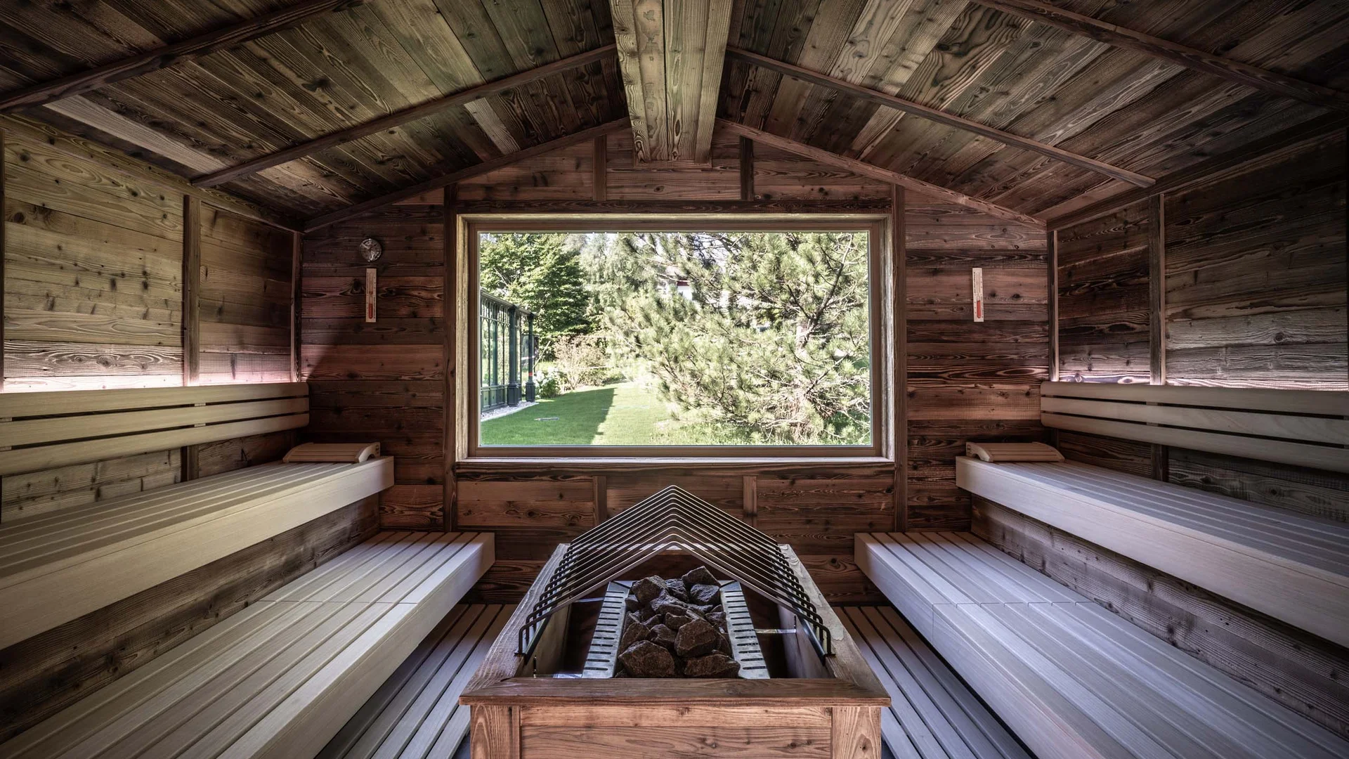 Wiesenhof – your spa hotel in Tyrol Interior of a wooden sauna with a large window showing greenery outside