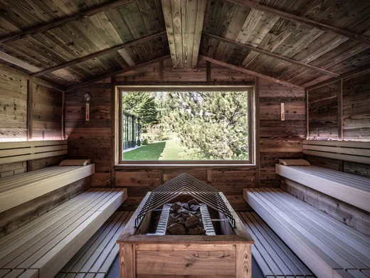 Wiesenhof – your spa hotel in Tyrol Interior of a wooden sauna with a large window showing greenery outside