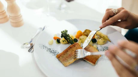 Wiesenhof from all perspectives Person cutting fried fish with vegetables on a white plate