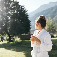 Wiesenhof – your spa hotel in Tyrol Woman in white bathrobe drinking tea in garden with mountain view in the morning