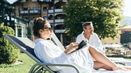 Wiesenhof from all perspectives Couple relaxing outdoors on lounge chairs in bathrobes by hotel
