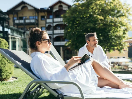 Wiesenhof – your spa hotel in Tyrol Couple relaxing outdoors on lounge chairs in bathrobes by hotel
