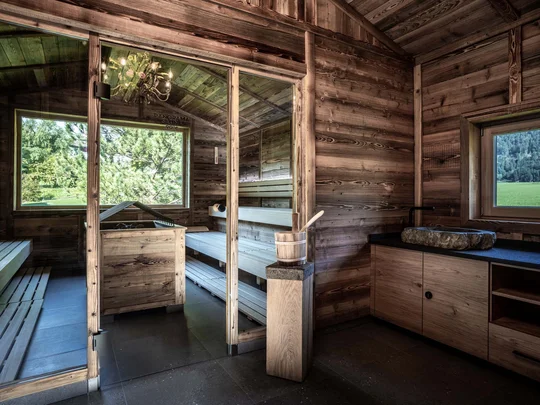 Wiesenhof – your spa hotel in Tyrol Wooden sauna with panoramic window overlooking green landscape