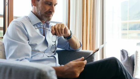 Wiesenhof from all perspectives Man sitting on sofa reading tablet, holding eyeglasses in hand