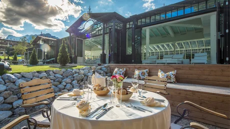 Wiesenhof from all perspectives Set outdoor dining table with chairs and glass building facade in sunlight