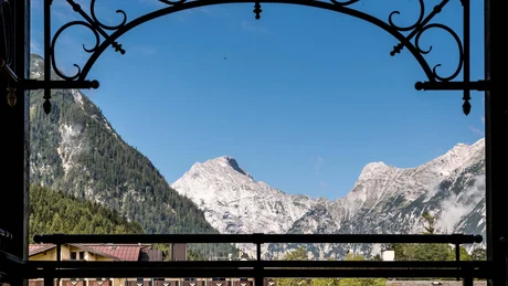 Wiesenhof from all perspectives View through ornate balcony railing of snowy mountain peaks under clear blue sky