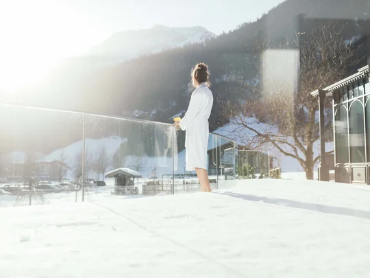 Wiesenhof – your spa hotel in Tyrol Woman in bathrobe on snowy balcony overlooking mountains in the morning