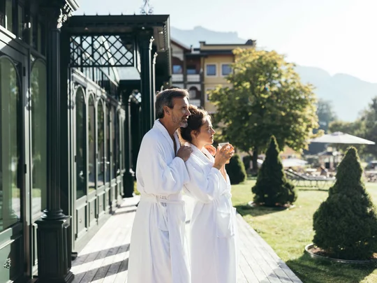 Wiesenhof – your spa hotel in Tyrol Couple in robes enjoying morning on terrace with garden and mountains