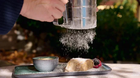 Wiesenhof from all perspectives Hand sprinkling powdered sugar on dessert served with berries on a plate