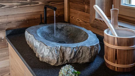 Wiesenhof from all perspectives Stone sink with running water faucet and wooden bucket on black countertop