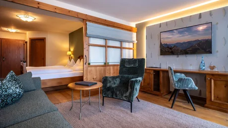 Wiesenhof from all perspectives Cozy hotel room with armchair, sofa, wooden desk, and visible bedroom area