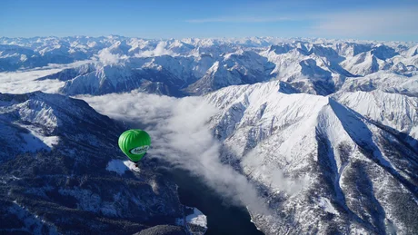 Wiesenhof from all perspectives Green hot air balloon flying over snowy mountains and a river valley