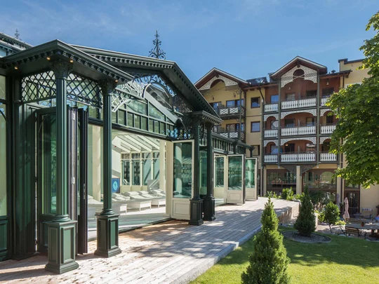 Wiesenhof – your spa hotel in Tyrol Modern conservatory and hotel building with terrace and garden under clear blue sky