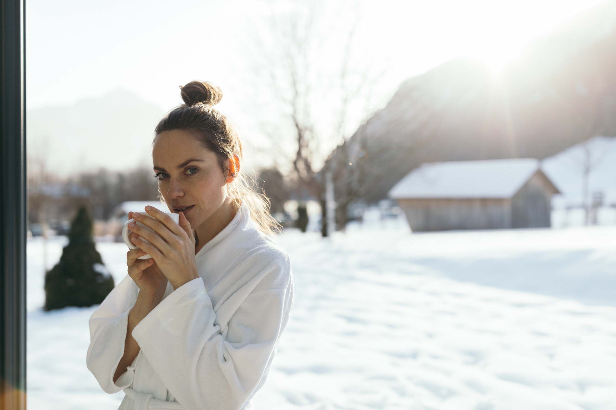 Wiesenhof – your spa hotel in Tyrol Woman in bathrobe drinking hot beverage outside in snowy landscape near cabin